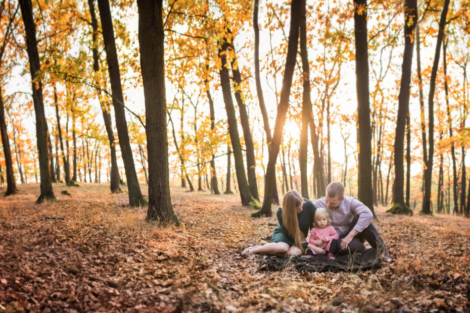 Malá rodina v podzimním lese se zapadajícím sluncem